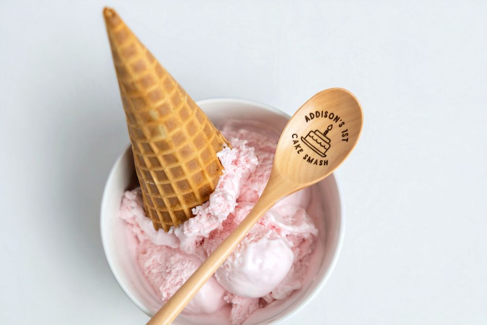 Pink strawberry ice cream in a white bowl with a waffle cone and personalized gold engraved spoon.