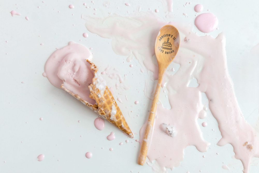 Melted pink strawberry ice cream cone with a wooden spoon on a light blue background.