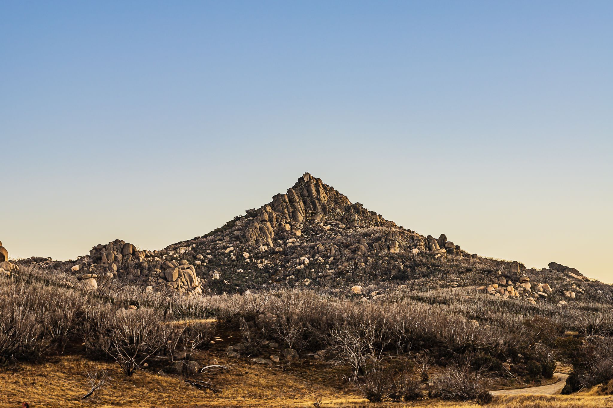 Rocky desert mountain peak with dry shrubs under a clear blue sky at golden hour.