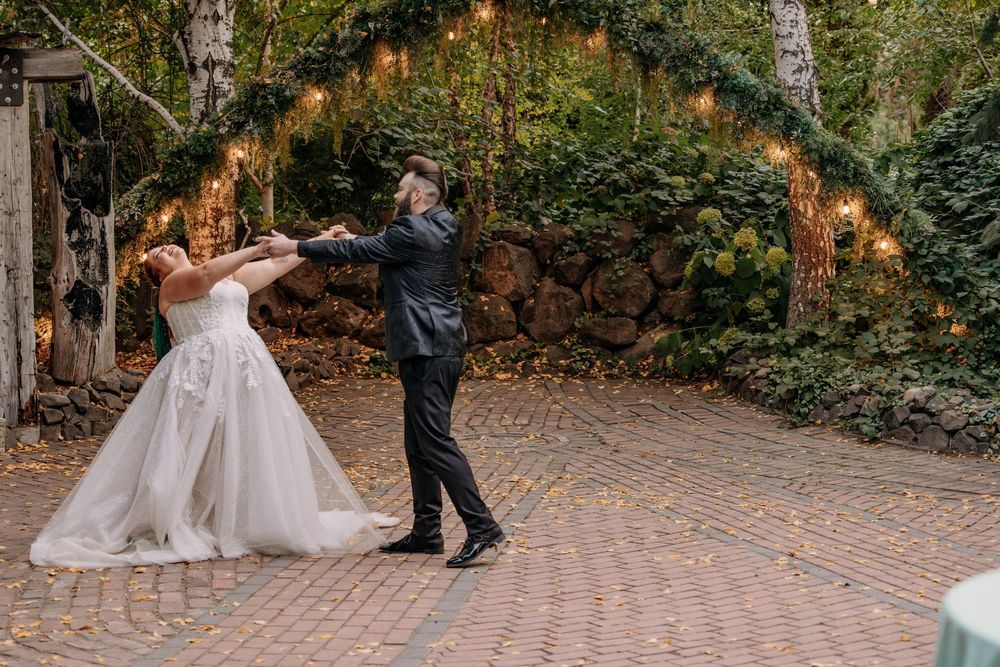 Bride and groom share first dance on brick patio surrounded by string lights and lush greenery.