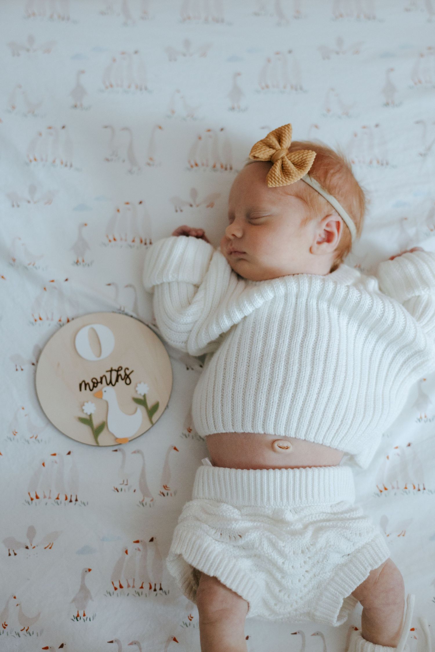 Sleeping baby wearing white knit sweater on patterned background.
