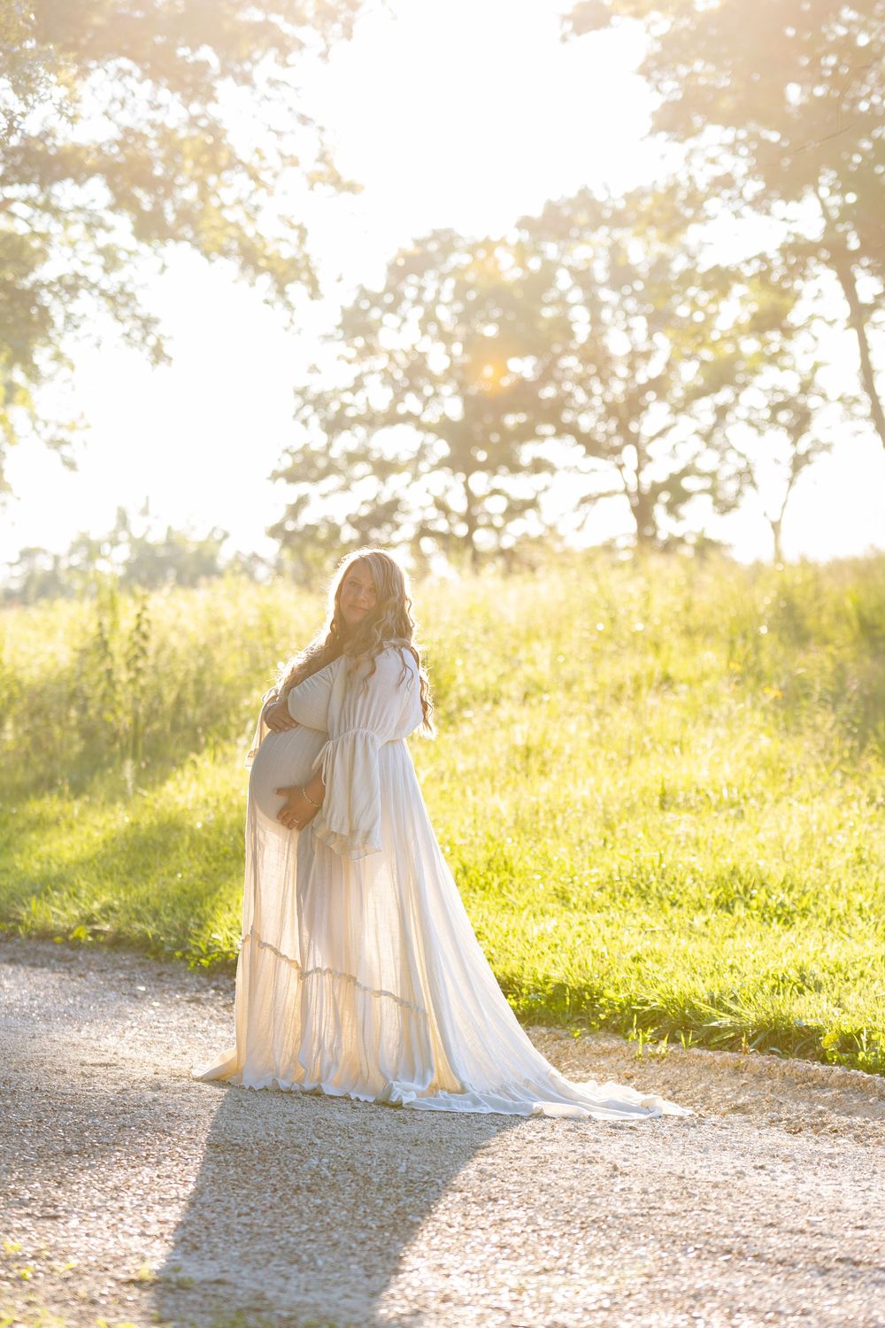 A dreamy couple in vintage white outfits walk along a sunlit path through a golden-lit meadow scenery.