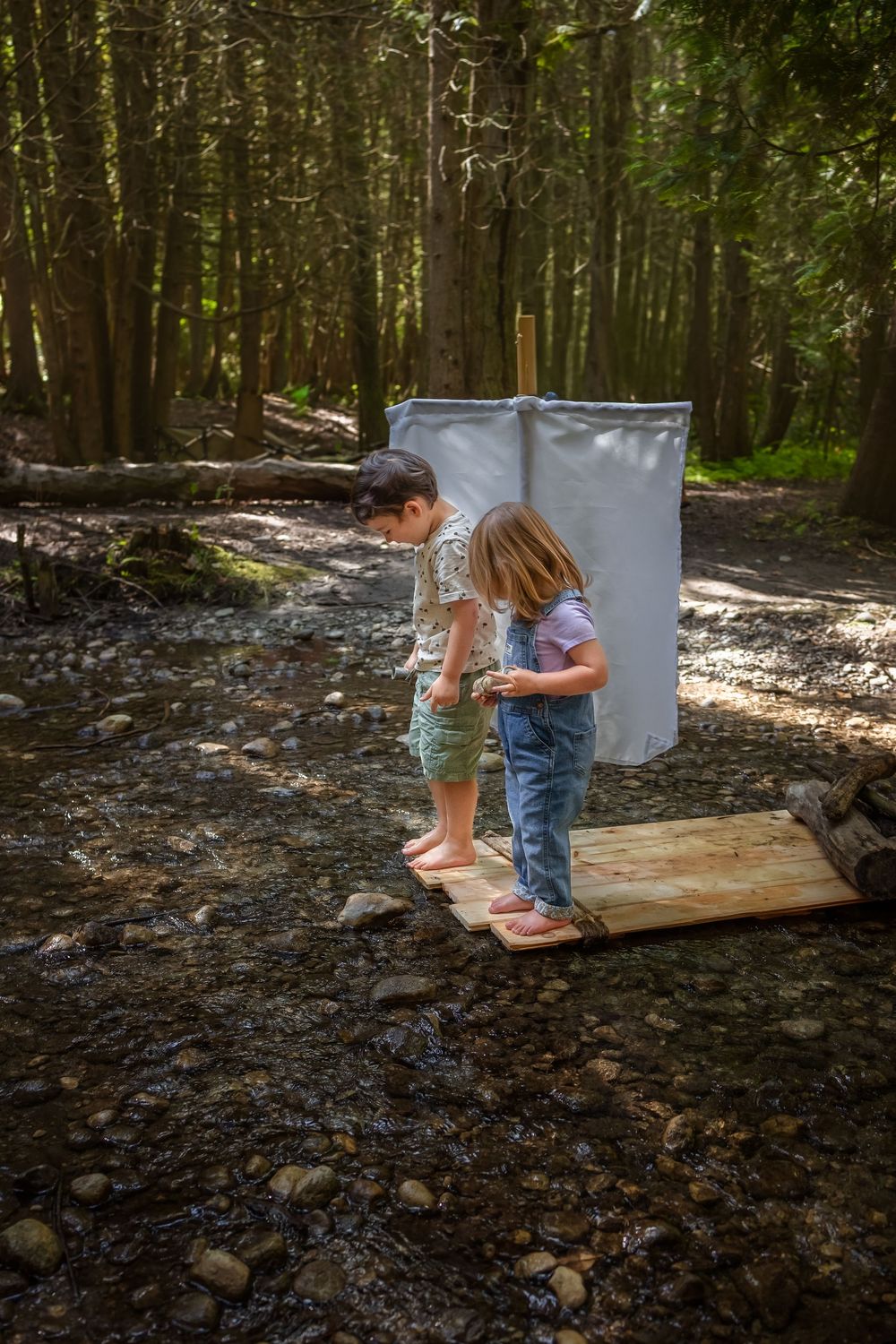 Children play on a raft on a creek in a wooded forest setting during a photo session.