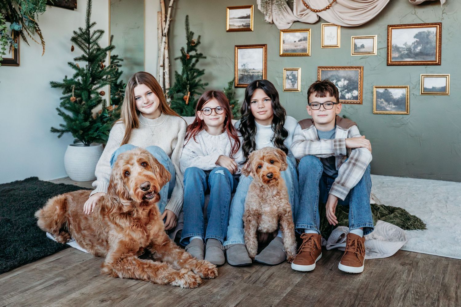 Family sitting on floor with dogs against grey wall with framed artwork.