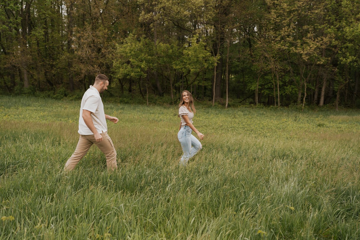 Playful couple runs through a green field on a sunny afternoon in Michigan.