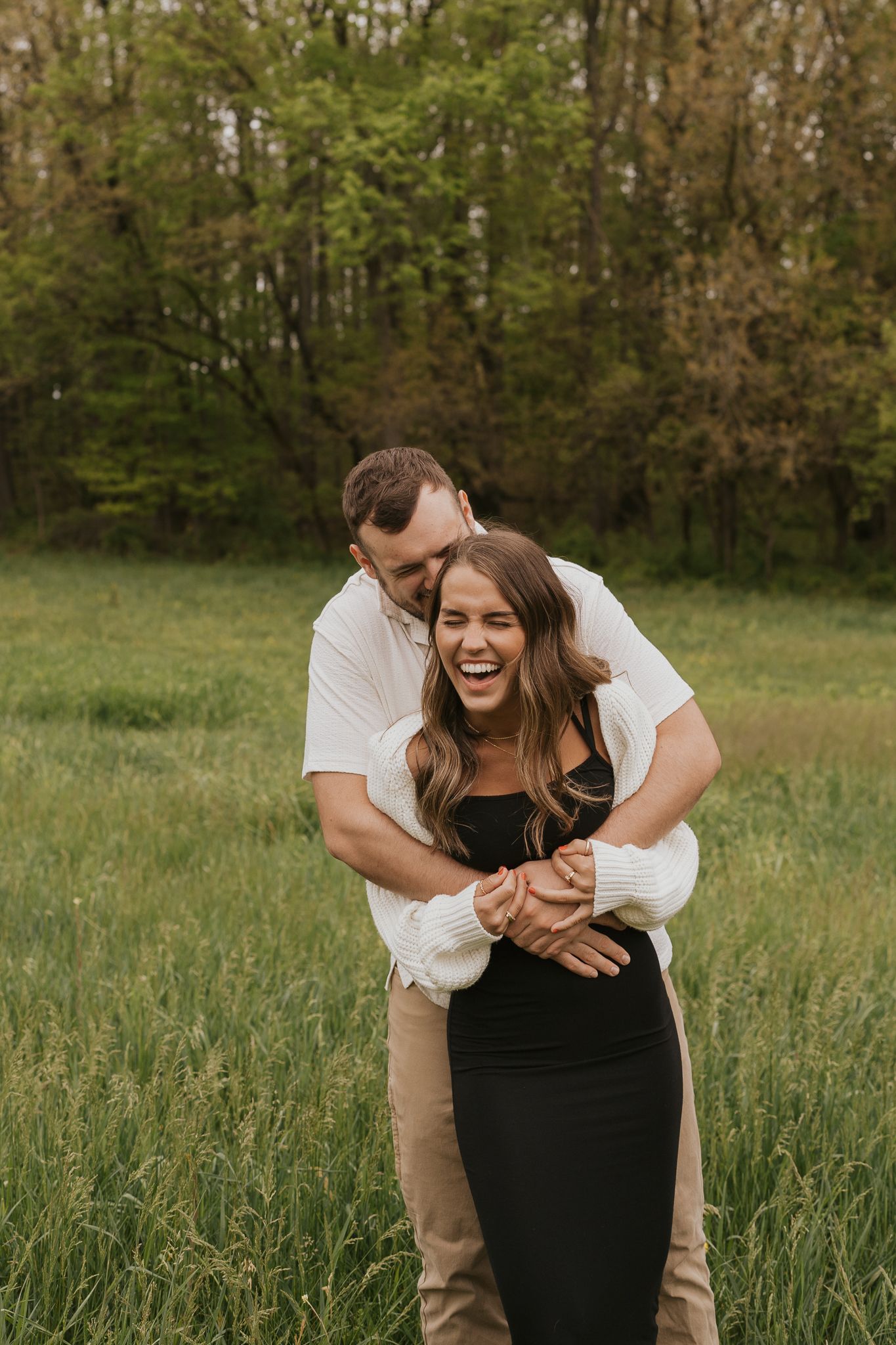 Couple laughs and embraces while enjoying a sunny day in a grassy meadow taken at Baily Photography in Michigan.