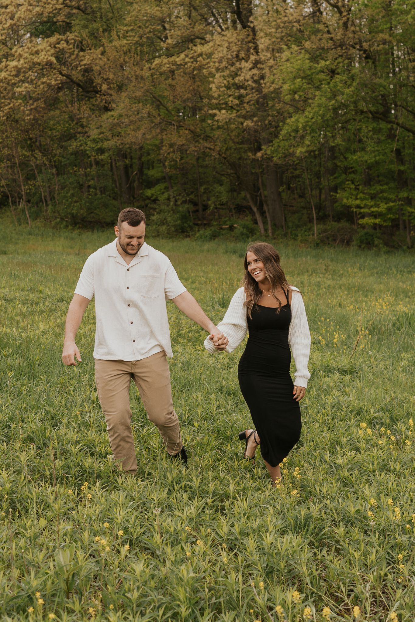 Couple playfully walks through a field of wildflowers on a summer day taken outdoors in Jackson MI.