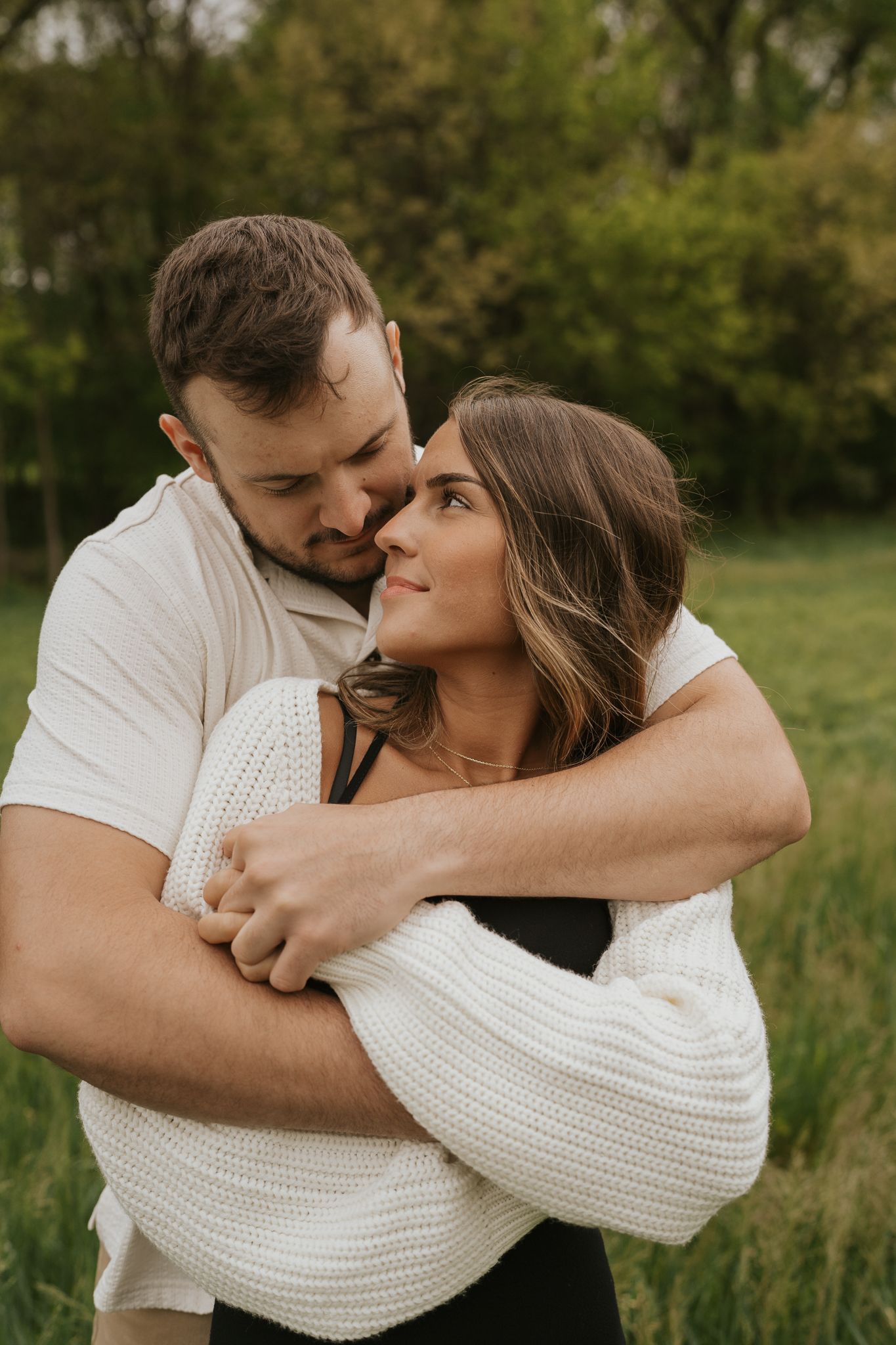 Intimate engagement moments captured between couple wearing white in green outdoor setting.