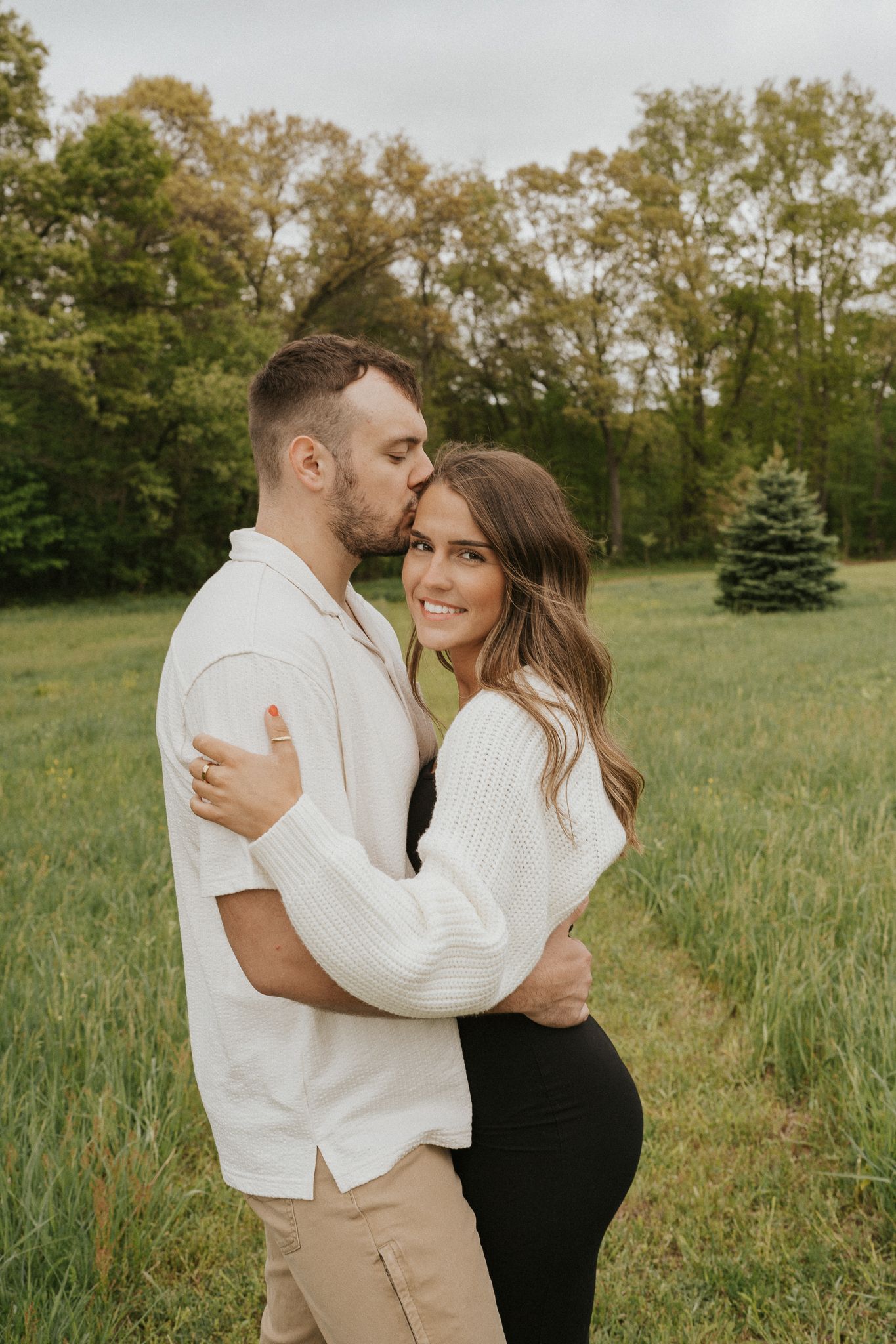 Couple in white and black outfits share romantic embrace in grassy field outside of Jackson MI