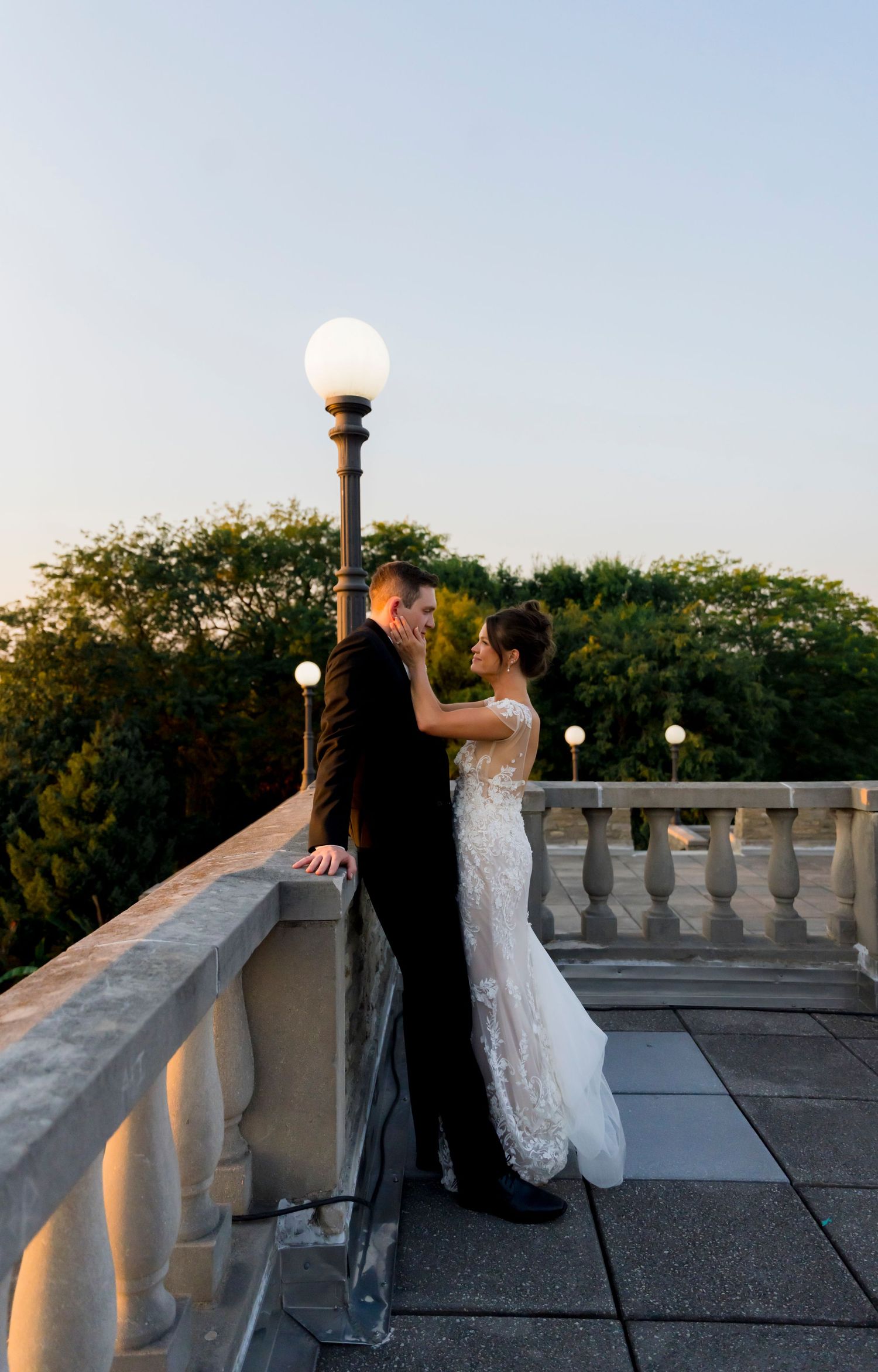 A romantic sunset silhouette of newlyweds on an elegant balcony with lamp posts.