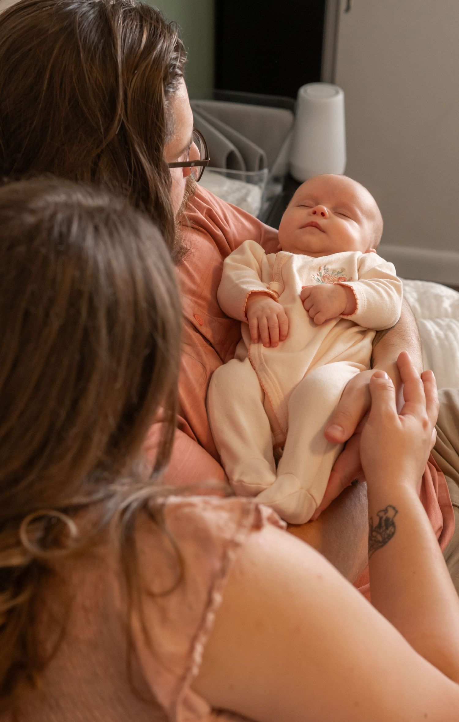 Mother gazing lovingly at her newborn baby dressed in white while sitting in bed.