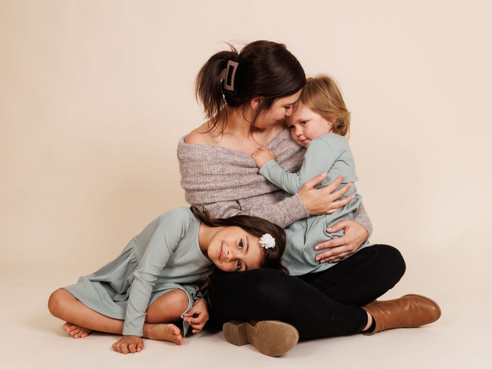 Mother and her two small daughters embracing together in a studio setting.