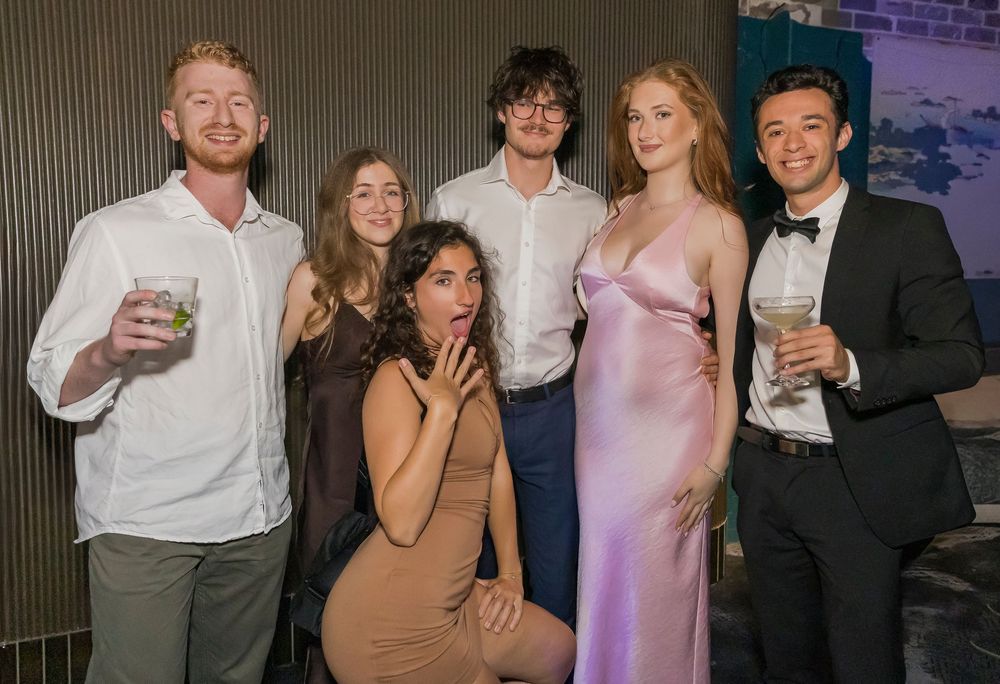 A group of friends pose together at a social gathering wearing formal attire and cocktail dresses.