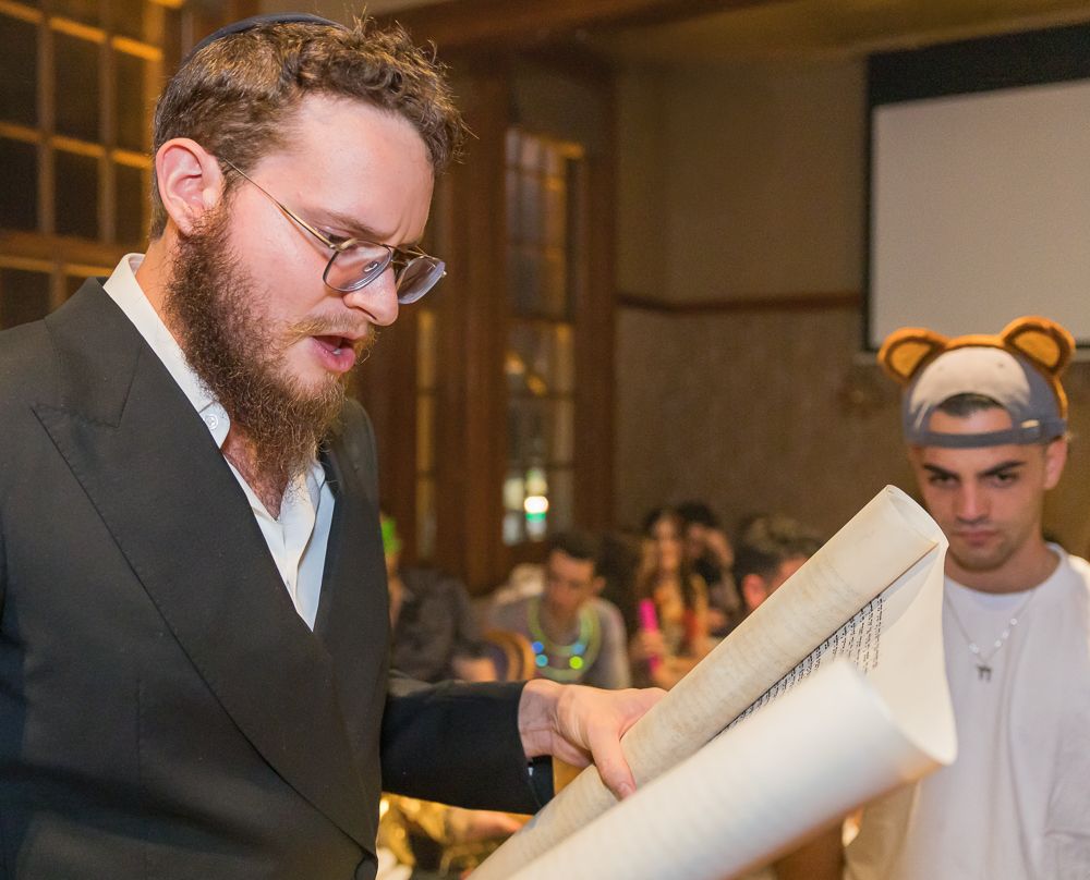 A person wearing glasses reads from a scroll during a religious ceremony.