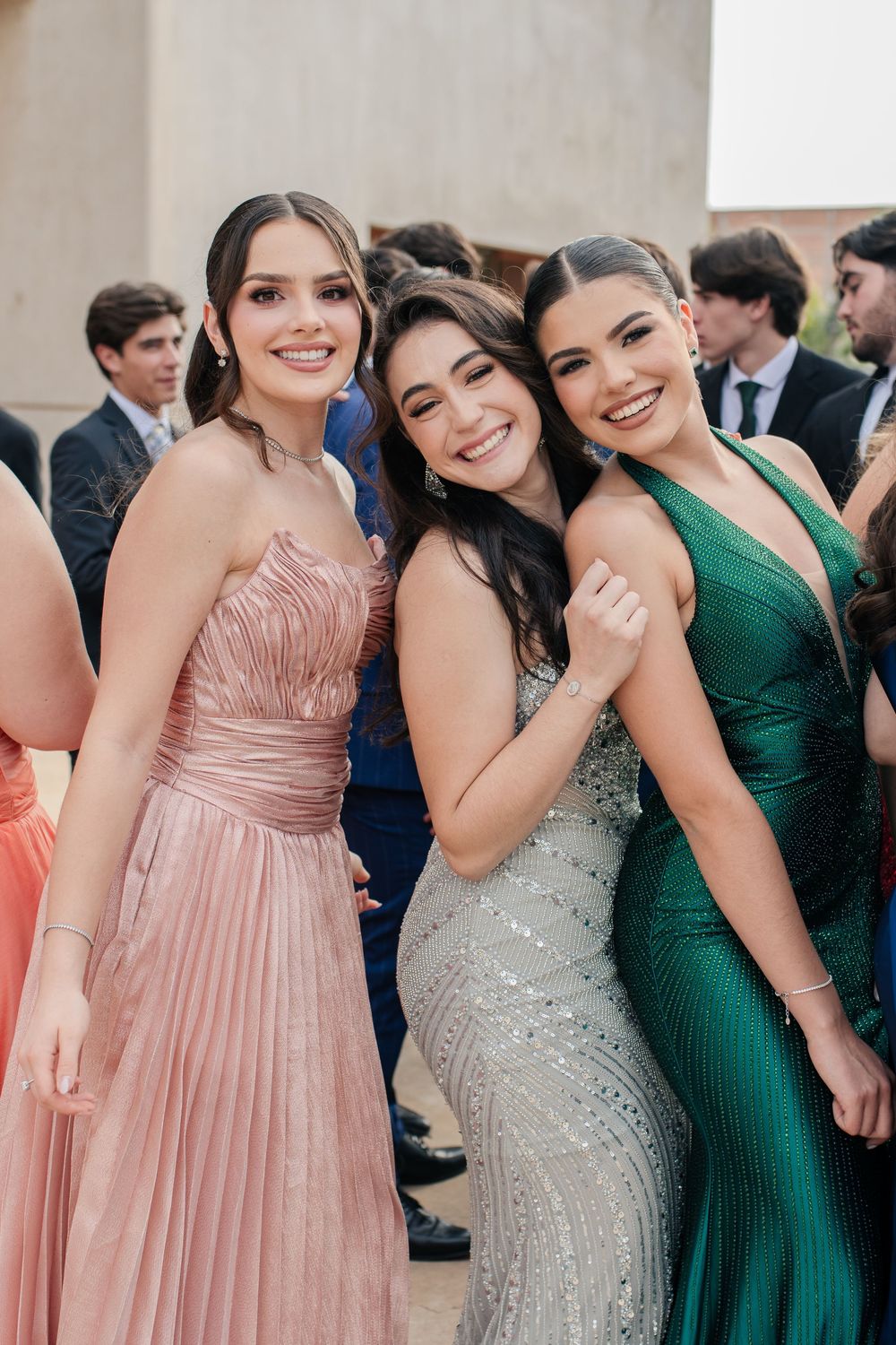 A group of formal event attendees wearing elegant dresses in shades of pink, green and sparkly silver pose together.