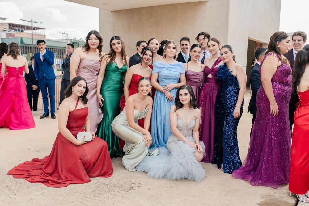 Formal group photo showing attendees in colorful evening gowns ranging from red to purple to blue.