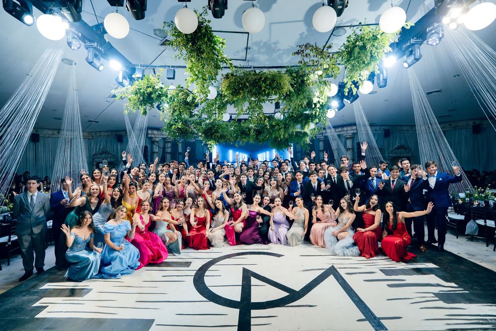 Large group gathered in an elegant venue with dramatic lighting and greenery for a formal event.