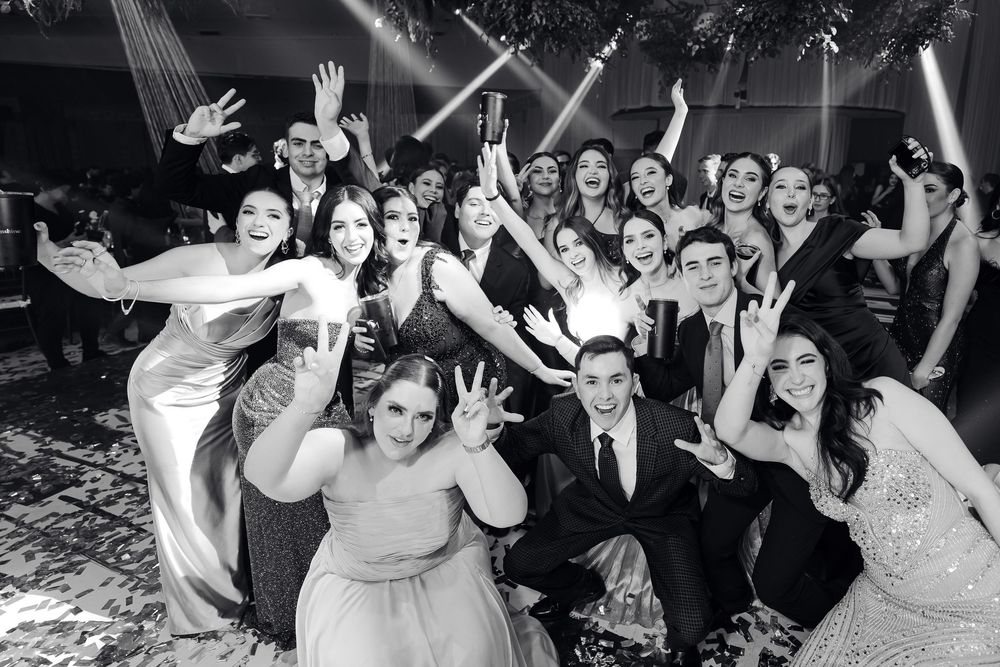 Black and white photo of party guests dancing and celebrating with raised arms at a formal event.