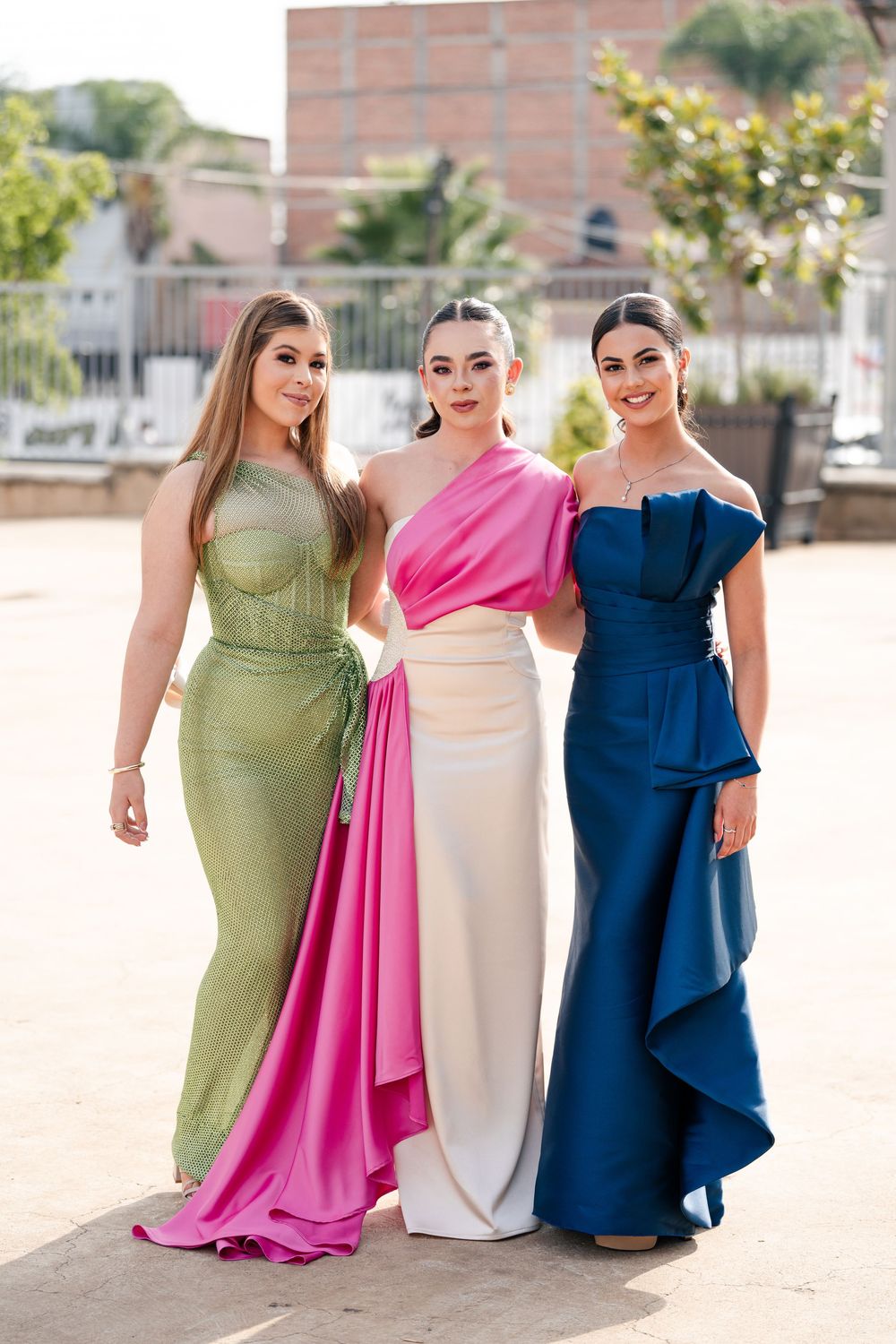 Bridesmaids wearing elegant gowns in green, pink, white and navy blue standing together outdoors.