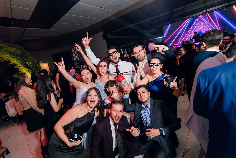 Energetic crowd dancing and celebrating at a nightclub party with colorful purple lighting effects.