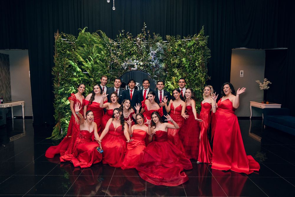 Large group in red formal attire posed in dark venue with dramatic lighting.