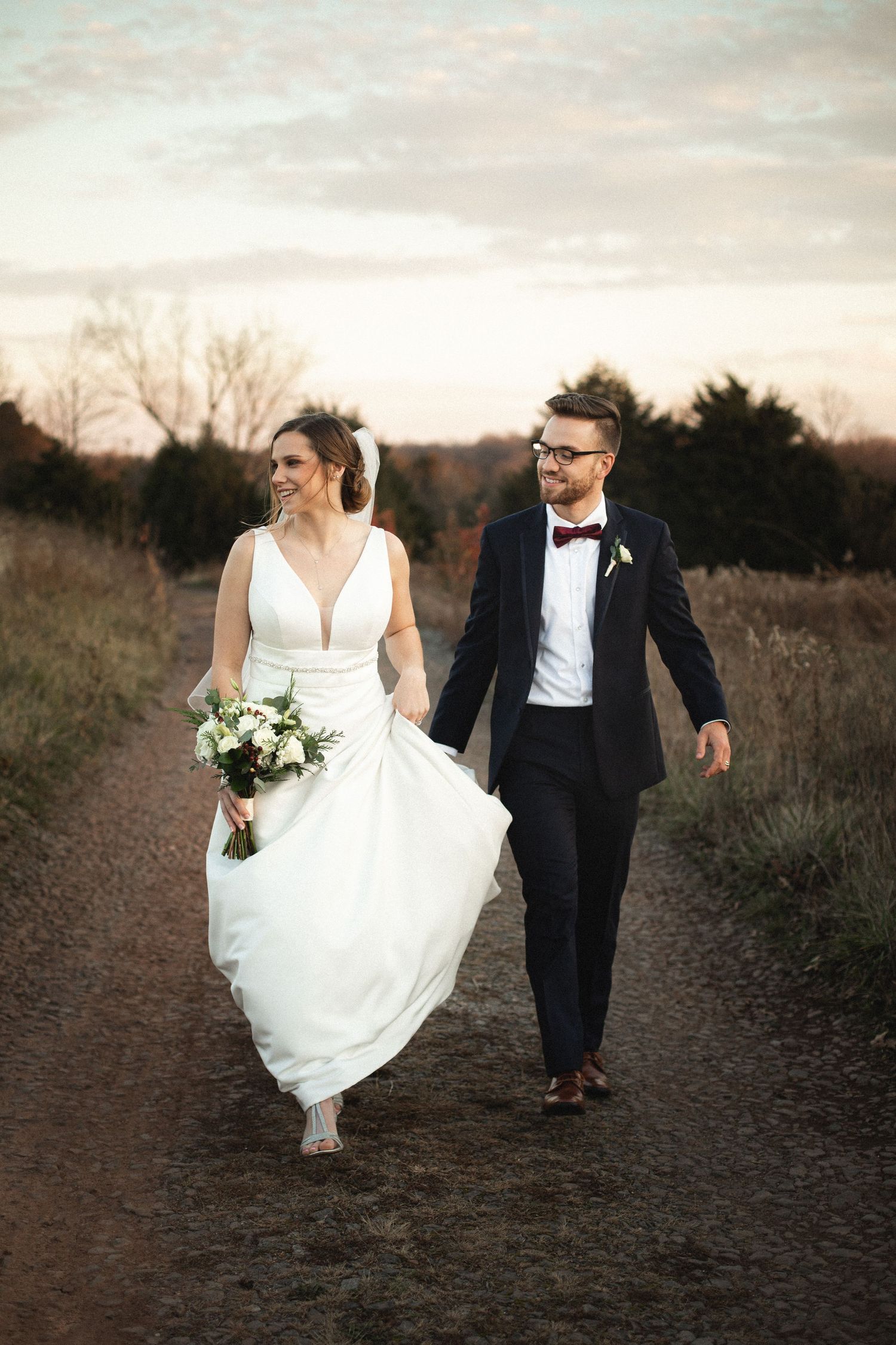 A couple running through a field at sunset in formal wedding attire.