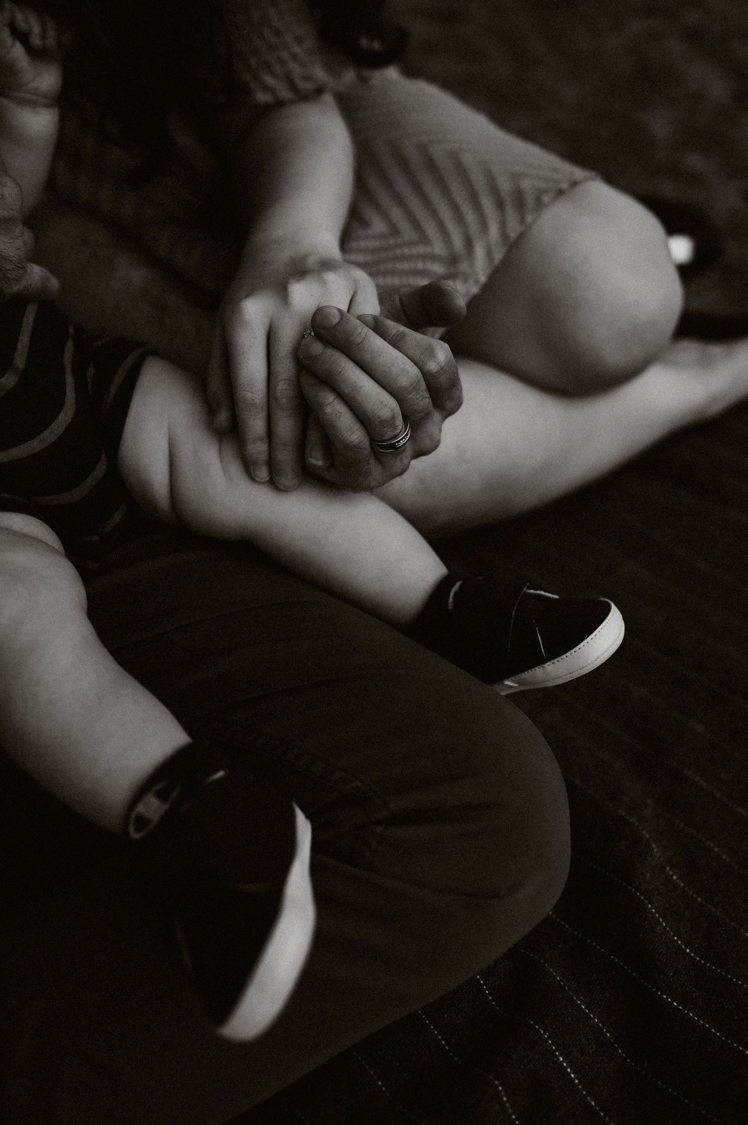 Close-up black and white photo of two people holding hands while sitting together.