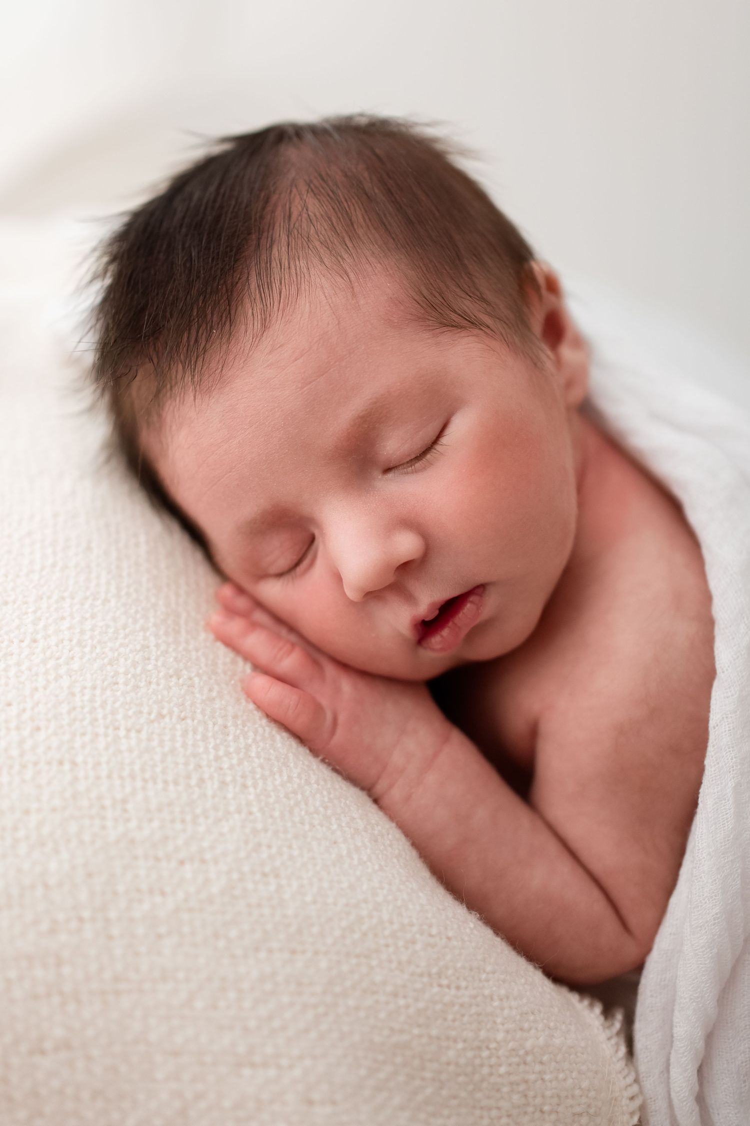 Peaceful newborn baby sleeping on soft cream textured blanket with hand near face.