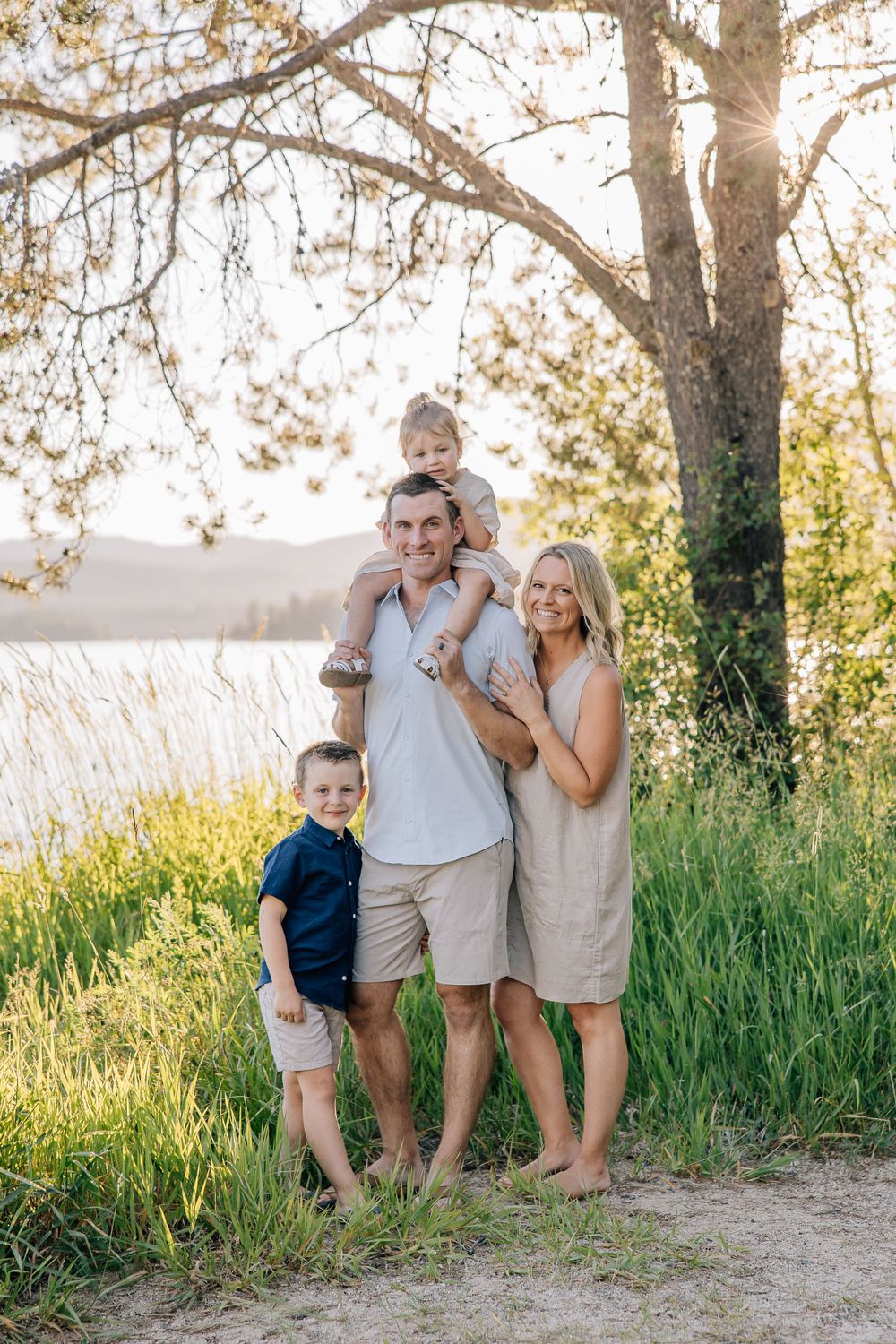 Family of four posing together by a lake during golden hour.
