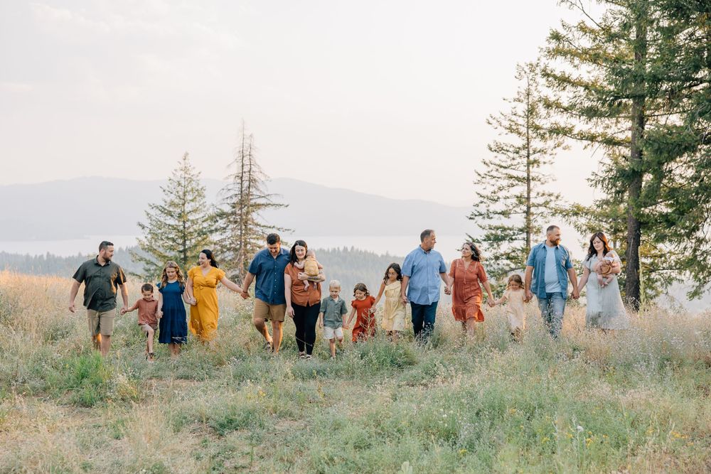 Extended family group walking together on a grassy hillside with evergreen trees in the background.