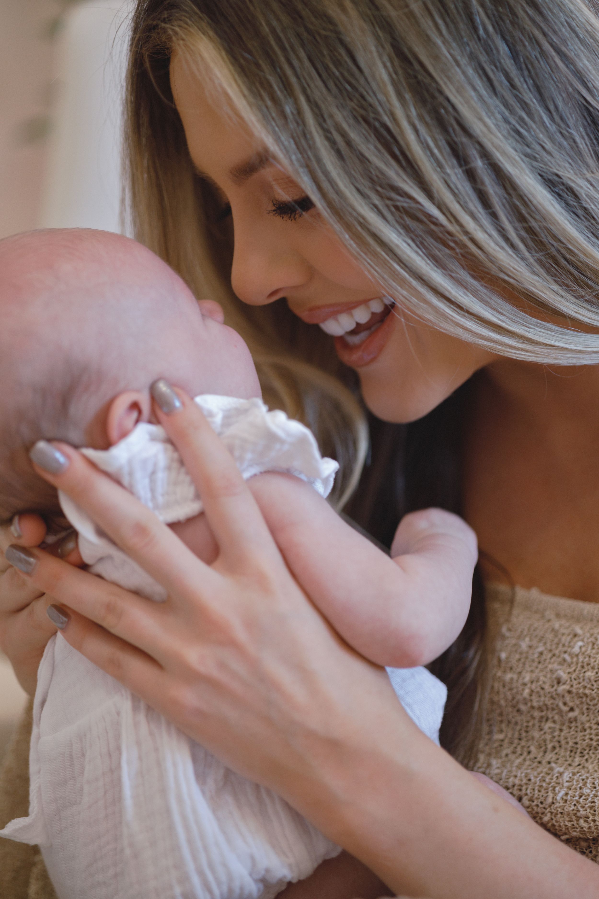 A tender moment between a parent and newborn baby wrapped in white, sharing a loving smile and gentle embrace.