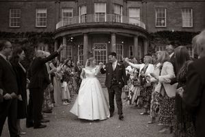 black and white image of a confetti exit, the bride and groom smiling at each other surrounded by happy friends and family.