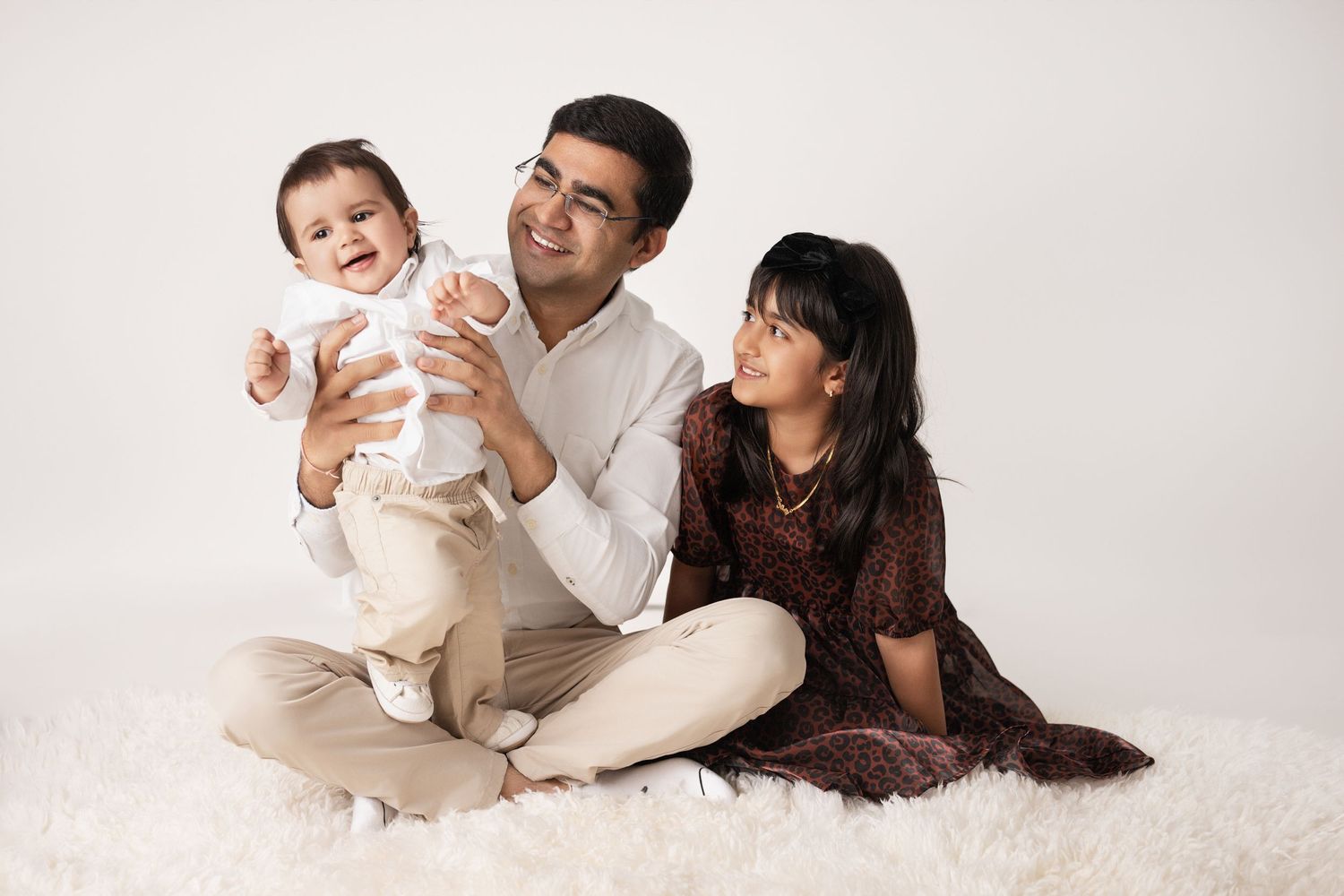 Family portrait session showing parents and baby in white outfits against light background.