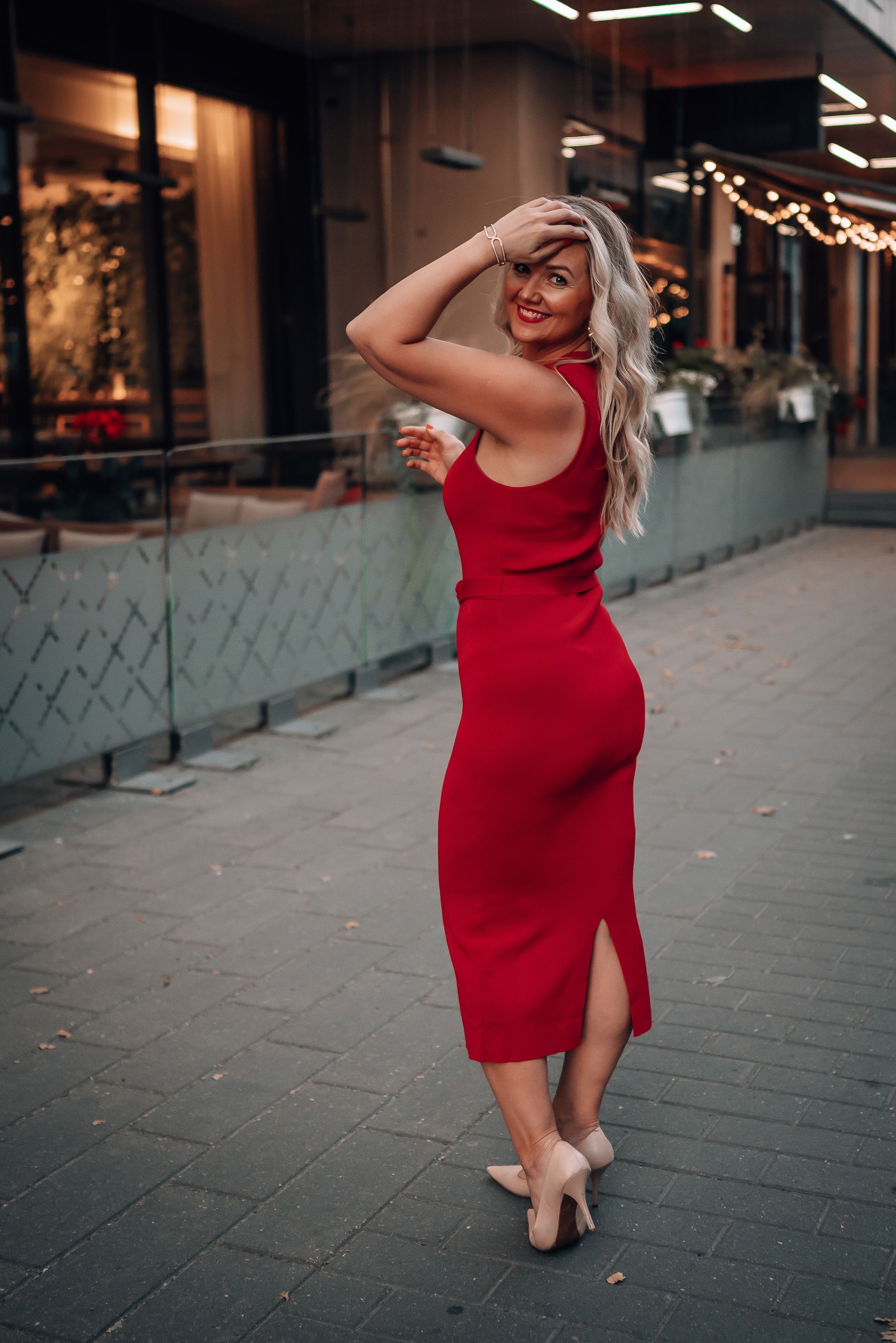 A woman in a red dress dances gracefully on a city sidewalk at dusk.