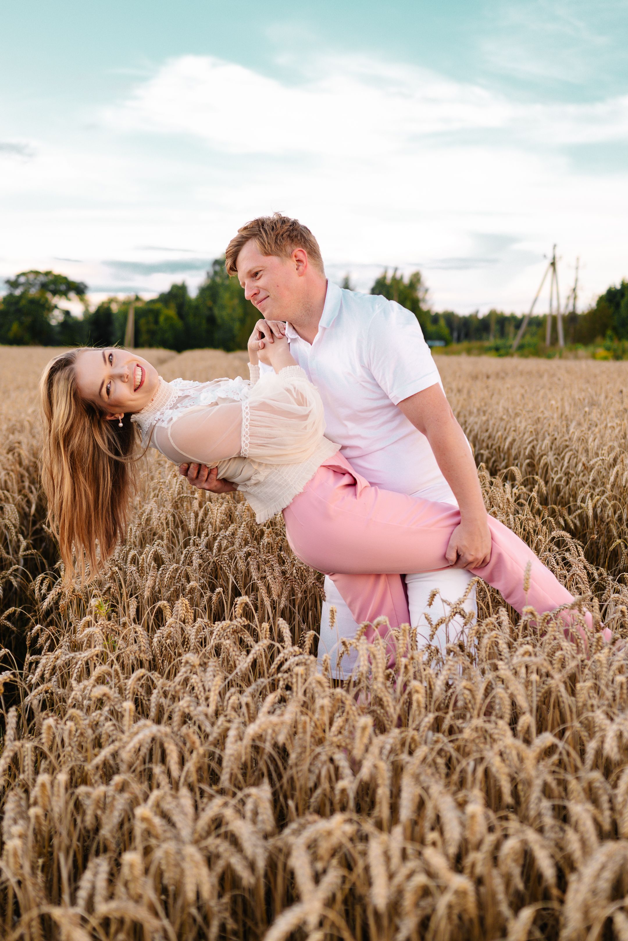 A couple shares playful moments together in a golden wheat field during sunset.