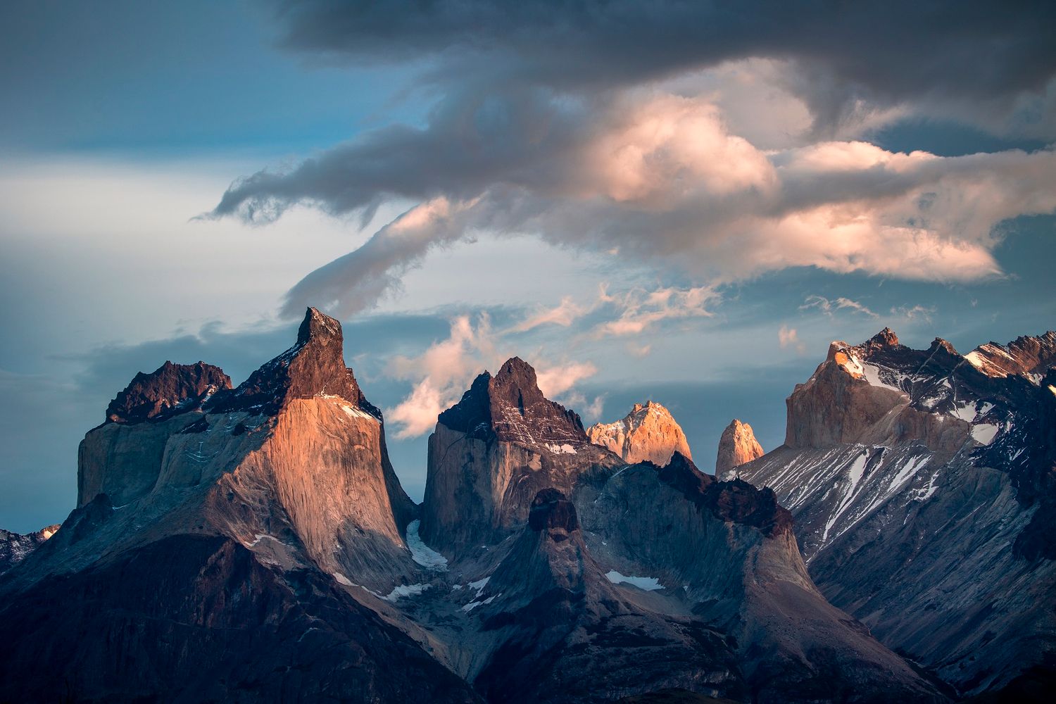 Dramatic sunrise illuminating the jagged peaks of Torres del Paine in Patagonia under stormy clouds.