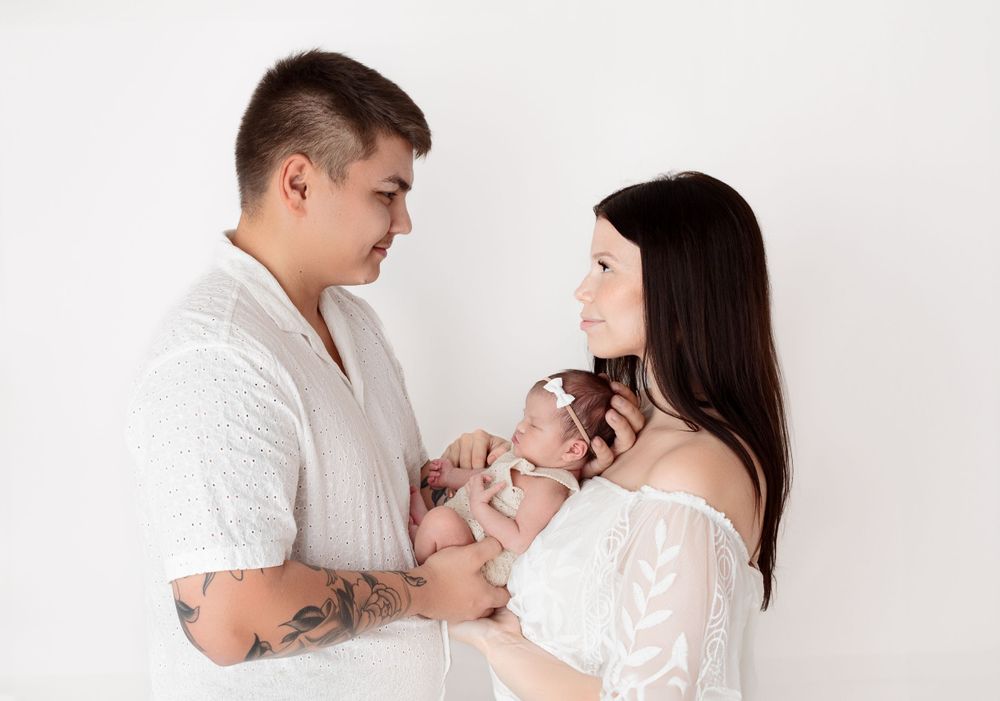Mother and father hold newborn baby together while she sleeps in their arms during newborn photography session in Victoria BC