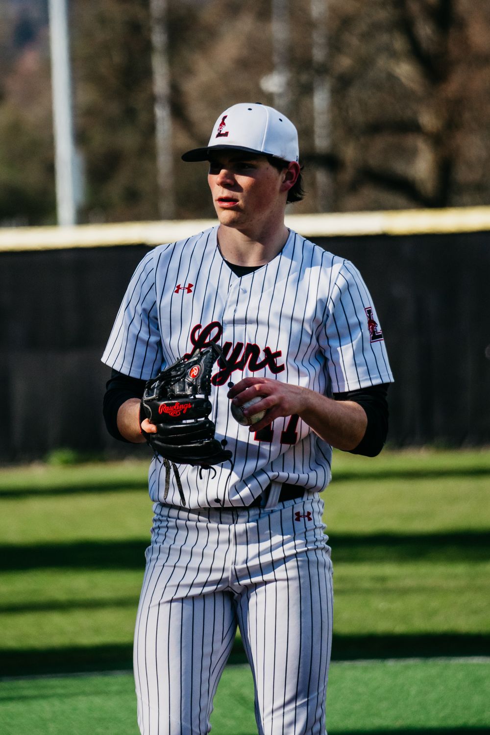 Baseball player in pinstriped uniform and glove stands ready on a sunny field during practice or game.