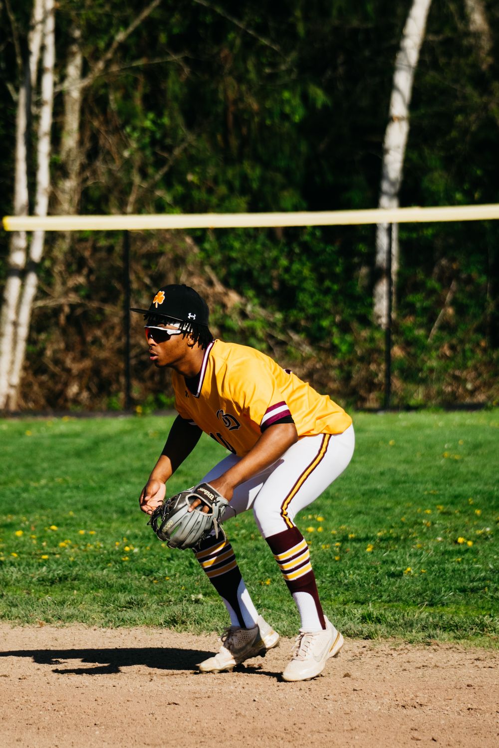 Baseball player in yellow uniform crouches in fielding position on dirt infield during sunny game.