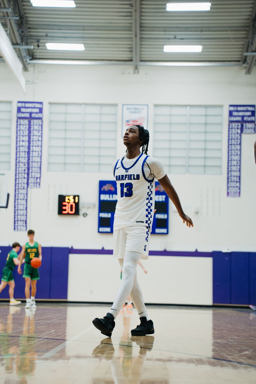 High school basketball players compete in a gymnasium with blue walls and white trim during an indoor game.