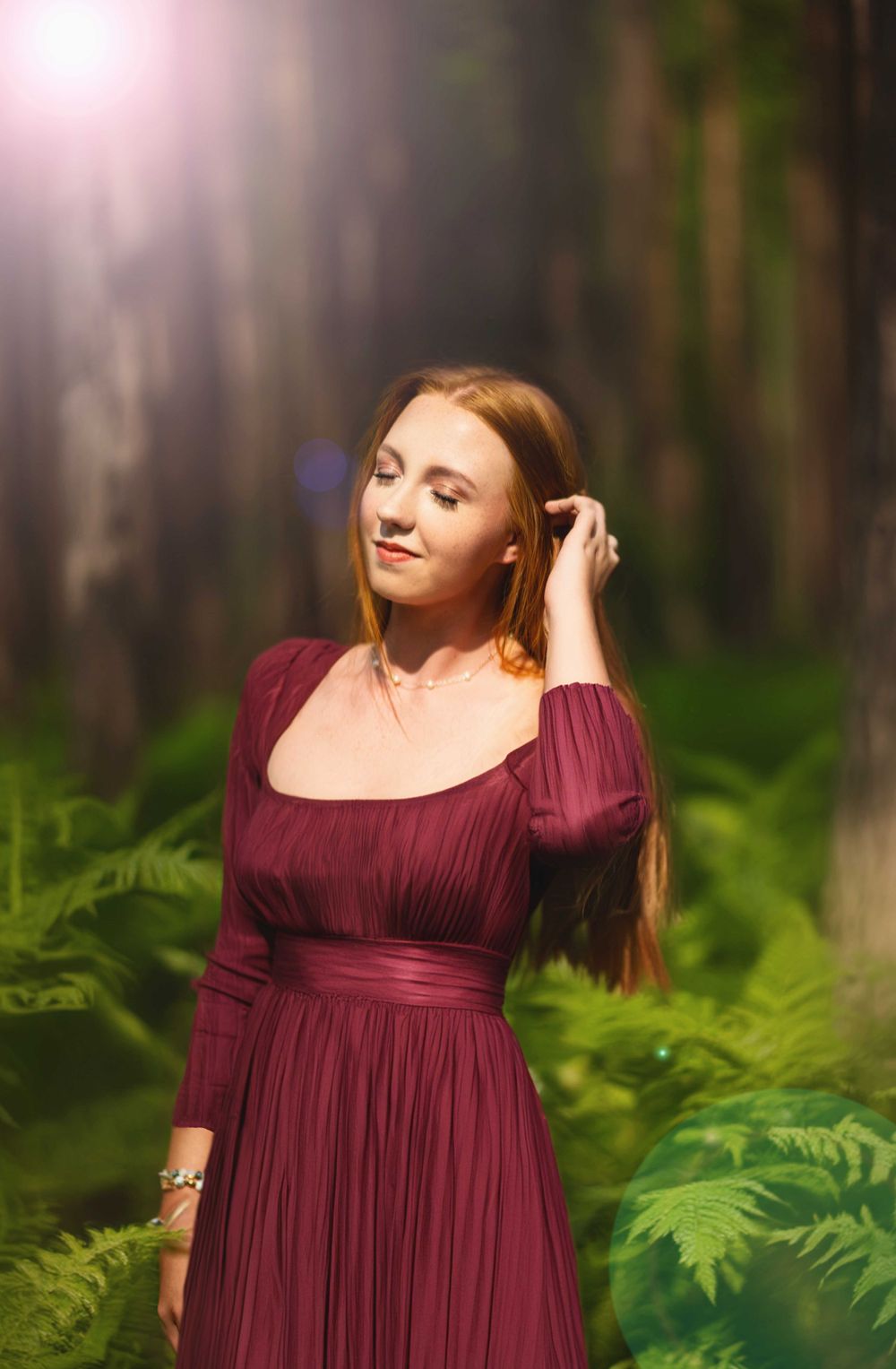 A dreamy forest portrait with soft lighting and burgundy dress among green ferns.