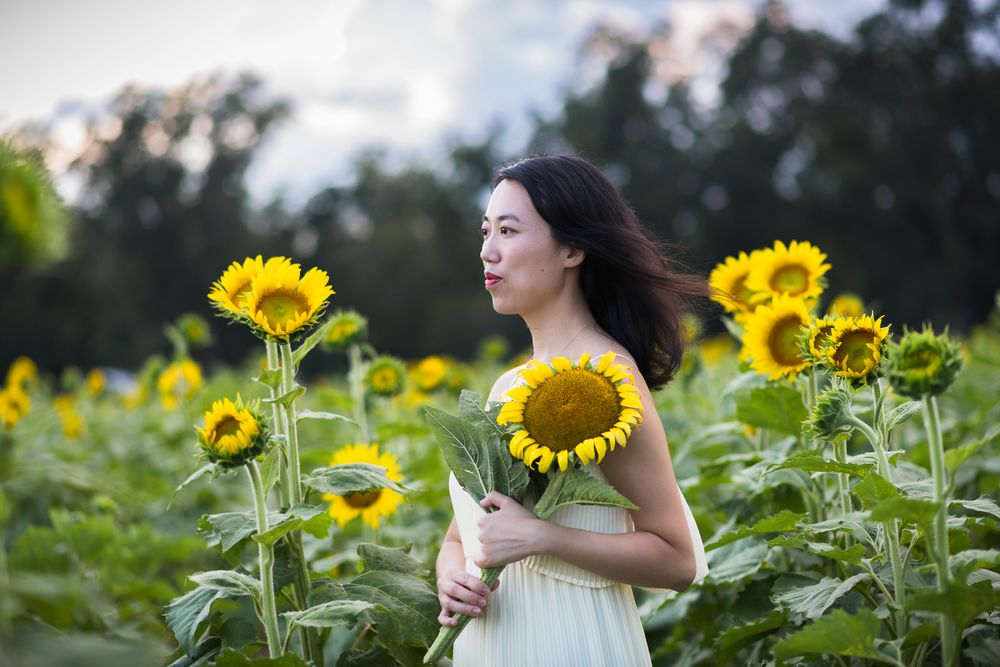 Ethereal portrait with wind-blown hair among towering sunflowers at dusk.