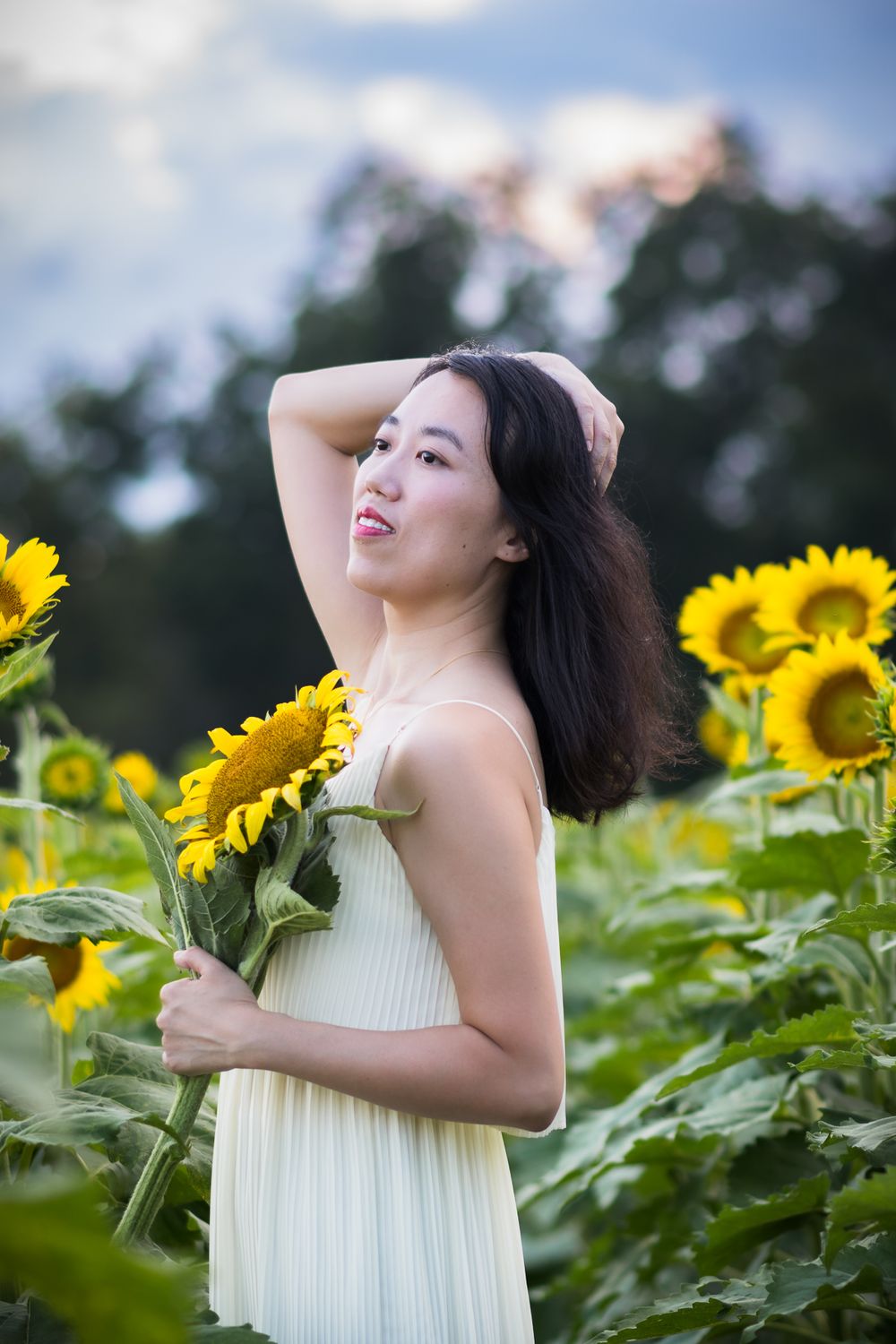 A woman in a white dress poses gracefully in a sunflower field on a summer day.
