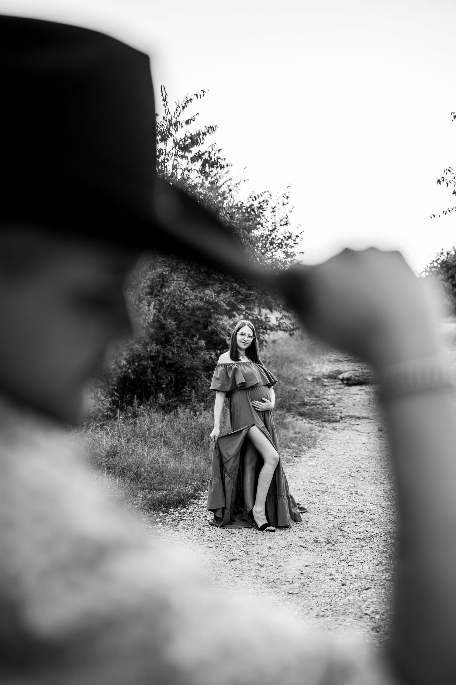 IMAGE OF A FORT WORTH PREGNANT MOM HOLDING HER BELLY WITH HER HUSBAND IN THE FORGROUND HOLDING HIS COWBOY HAT FOR THEIR MATERNITY PORTRAITS