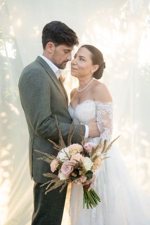 Romantic wedding portrait with couple embracing in soft sunlit garden setting.