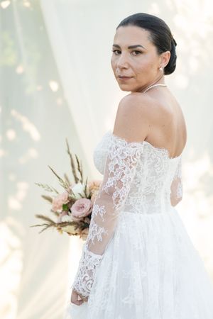 Elegant bridal portrait showing detailed lace wedding dress and bouquet in natural light.