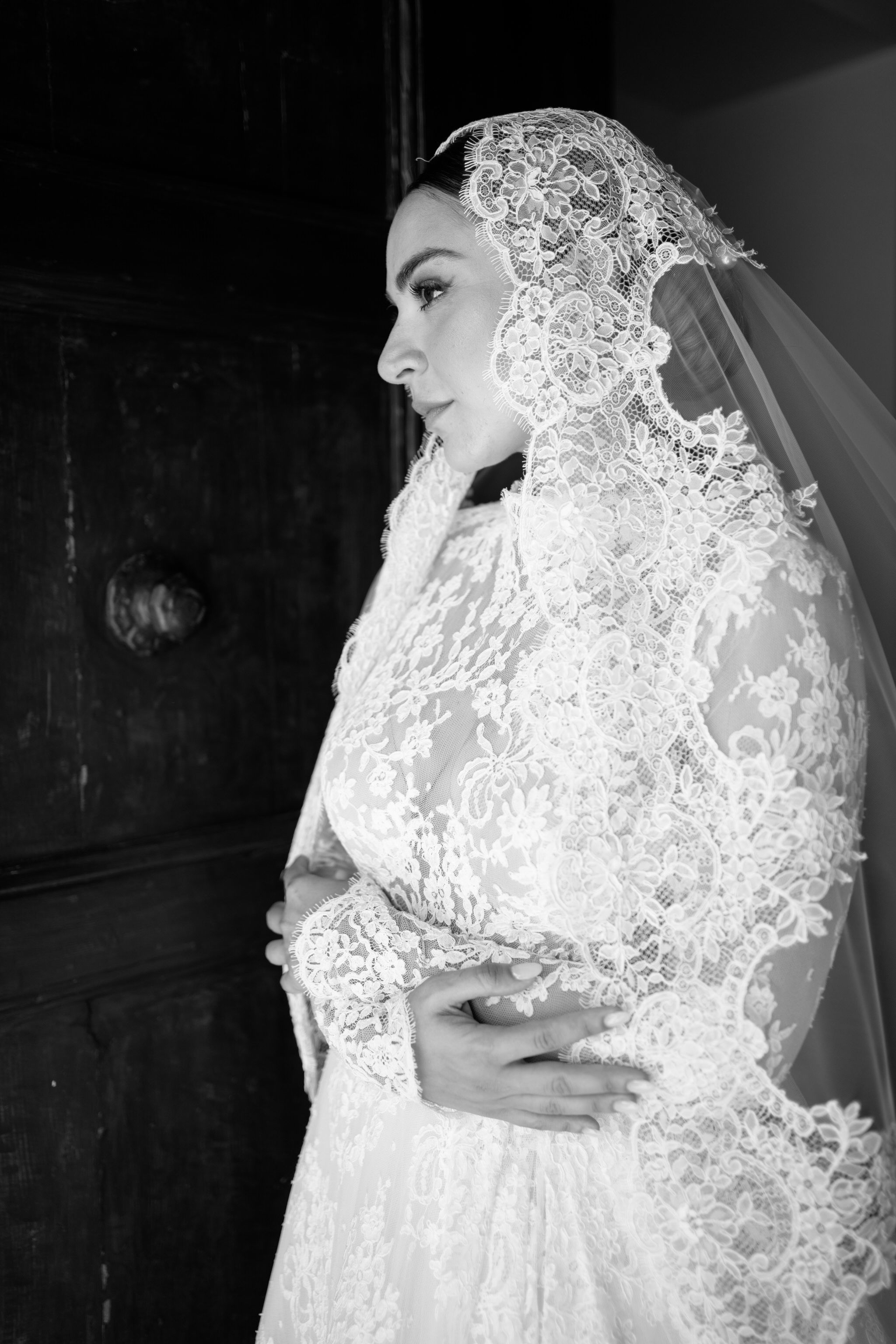 Dramatic black and white portrait of bride wearing intricate lace veil.