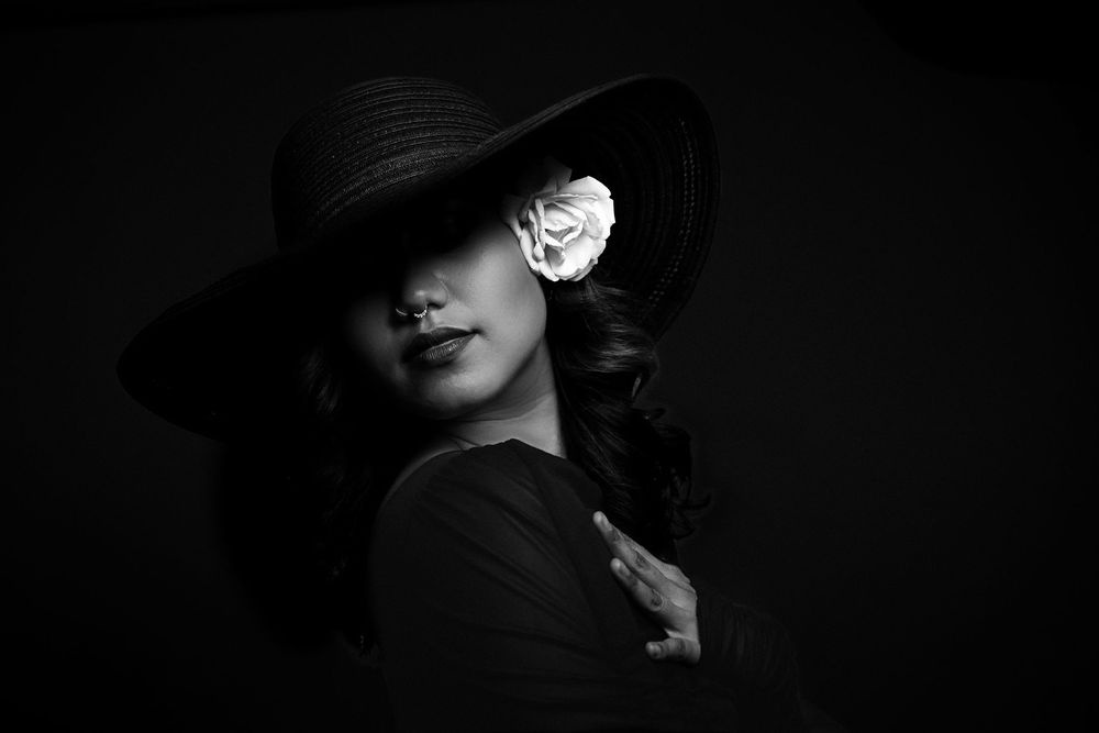 Dramatic black and white portrait of a figure in a wide-brimmed hat casting shadows across their face.