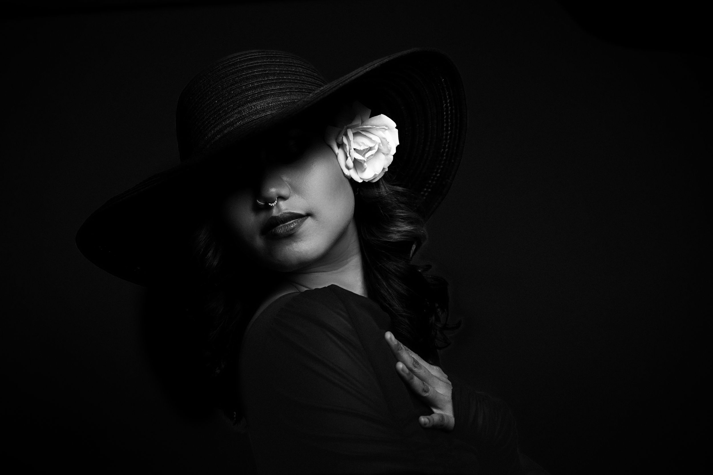Dramatic black and white portrait of a figure in a wide-brimmed hat casting shadows across their face.