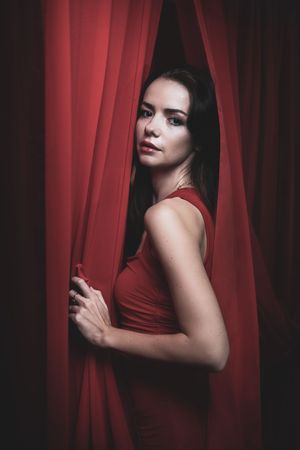 A dramatic photo series showing a figure posing behind red velvet curtains in a dark theatrical setting.